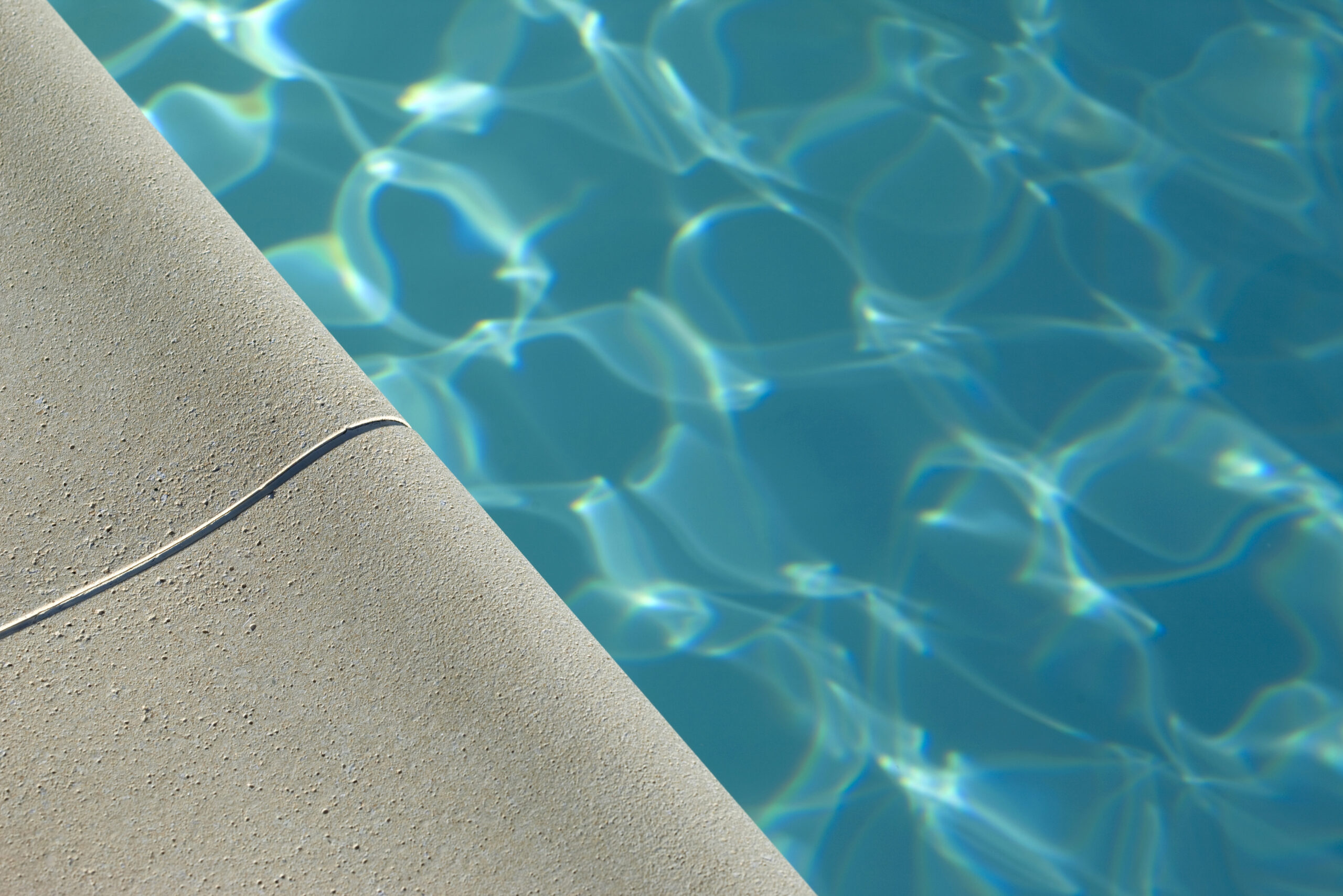 Changer sa toile de piscine : margelle de béton bordant une eau bleue claire et ondulée