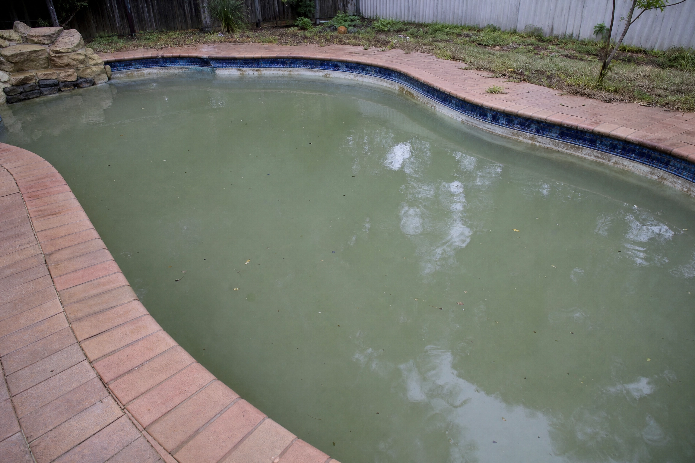 Eau de piscine trouble et grisâtre dans une piscine creusée bordée de briques et de mosaïque bleue