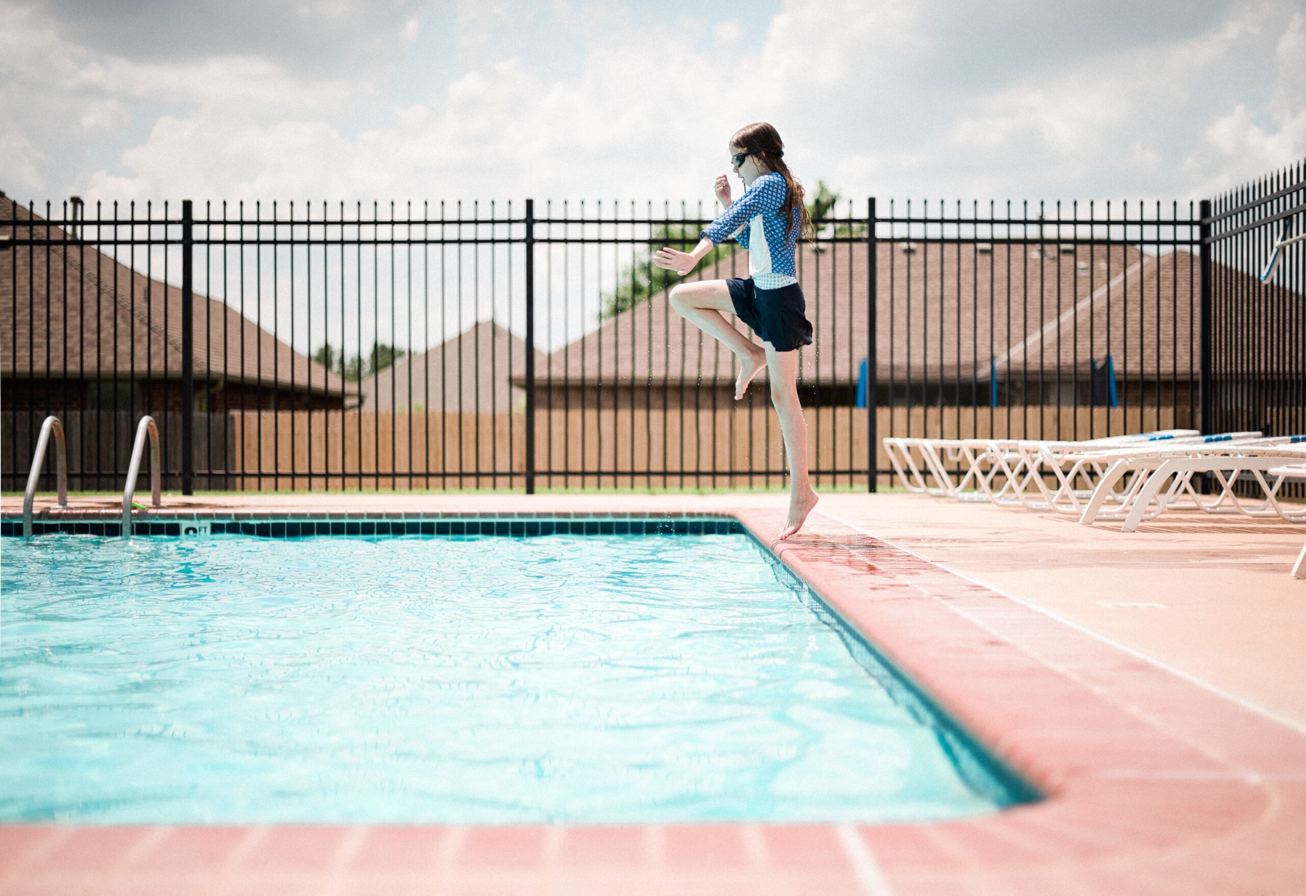 Enfant sautant dans une piscine entourée d'une clôture en fer conforme à la réglementation de clôture de piscine