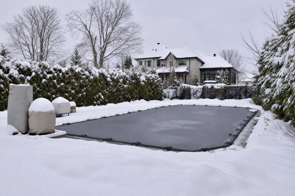 Piscine creusée recouverte d'une toile d'hiver sous la neige, une façon de protéger sa piscine du gel.