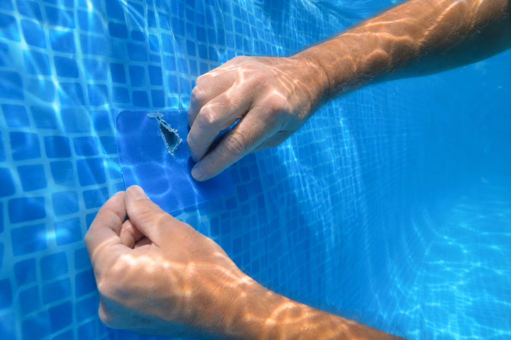 Mains appliquant une pièce autocollante sous l'eau pour réparer une toile de piscine perforée.