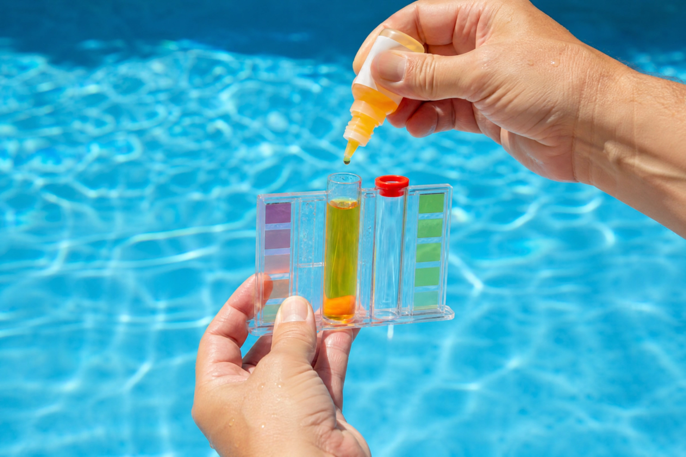 Mains ajoutant quelques gouttes de réactif dans une trousse d'analyse d'eau à côté d'un bassin, une étape essentielle pour vérifier le pH de piscine
